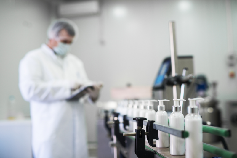 Cosmetic Solutions Quality Assurance image features a quality control officer inspecting skincare bottles on a manufacturing line